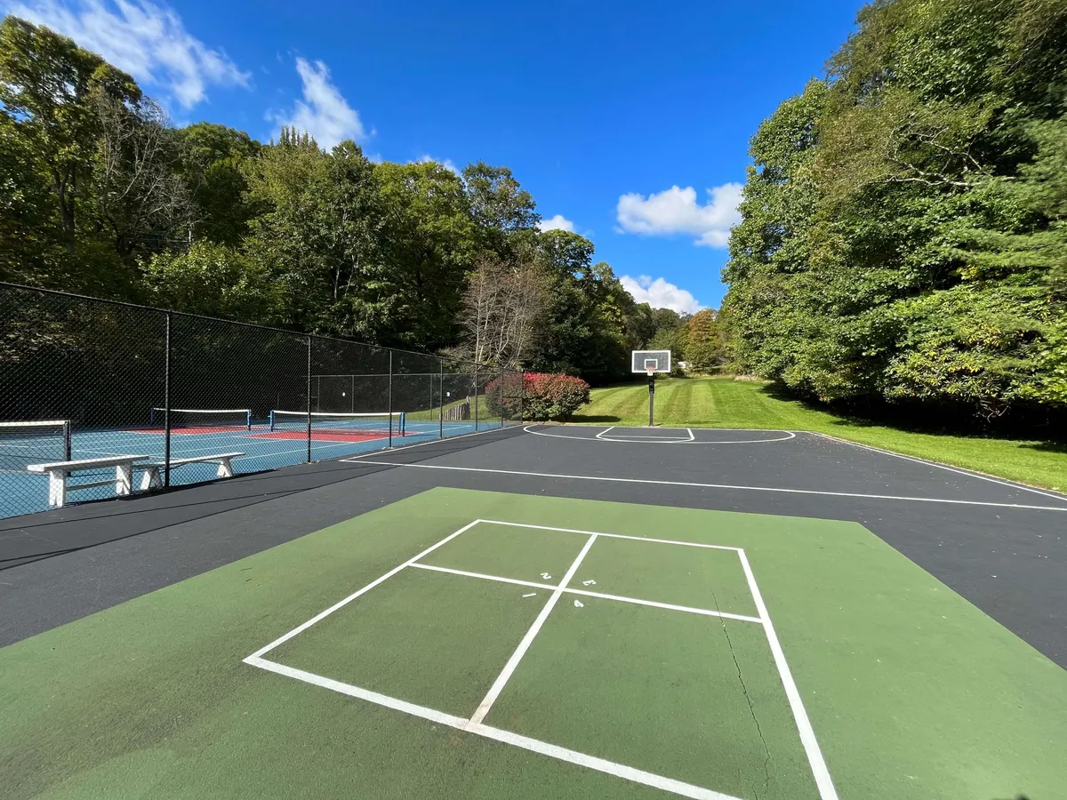 The image presents a vibrant recreational area with basketball and tennis courts surrounded by lush greenery and blue skies. It suggests a lively, energetic atmosphere where guests of all ages can enjoy sports and recreation together.