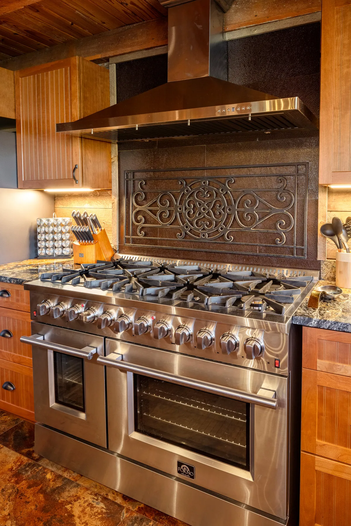 A close-up of the cooking area showcasing a stainless steel stove, ornate backsplash, and wooden cabinetry. The space combines vintage style with modern cooking convenience, emphasizing both function and charm.