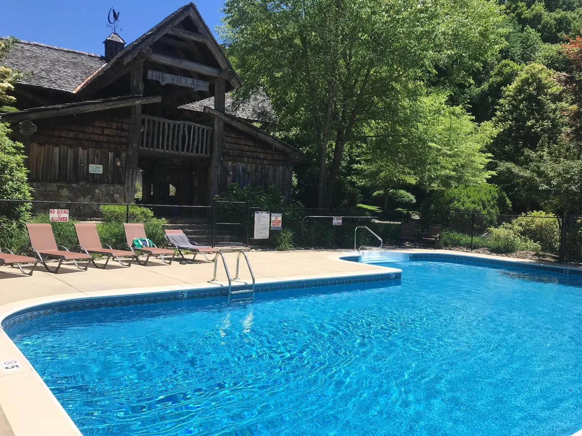 A tranquil swimming pool bordered by a wooden building and lounge chairs is nestled amidst lush greenery. The inviting pool hints at relaxation and social gatherings for guests seeking comfort after a day outdoors.