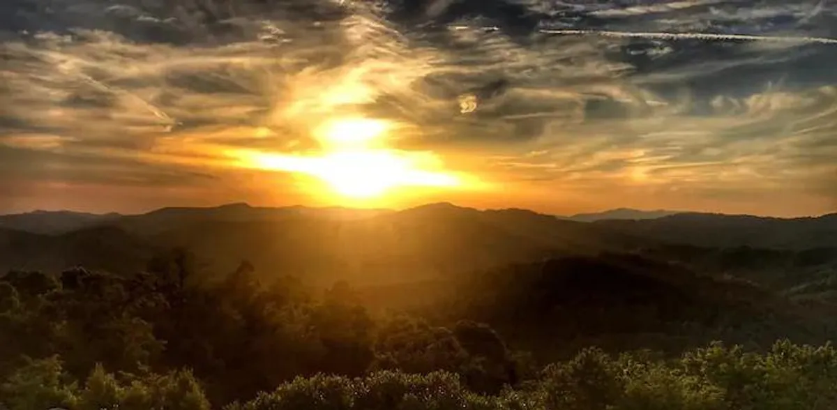 A breathtaking mountain range bathed in the glow of sunset, with clouds adding dramatic effect to the sky. The scene evokes peace and natural beauty, offering a sense of the surrounding landscape that frames the retreat experience.