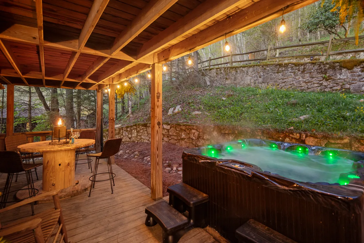 This exterior image features a hot tub on a spacious deck, accompanied by a wooden table and strung with charming string lights. The setting is surrounded by nature, evoking a sense of privacy and tranquility ideal for relaxation or social gatherings.