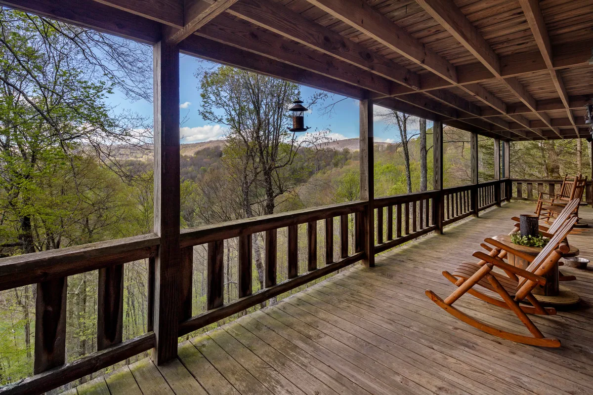 A set of classic rocking chairs are positioned along a wooden deck with hanging lanterns overhead. The deck overlooks rolling hills and distant mountains, inviting you to enjoy sunrise or sunset in peace. The furnishings and railings evoke comfort and encourage lingering outdoors.