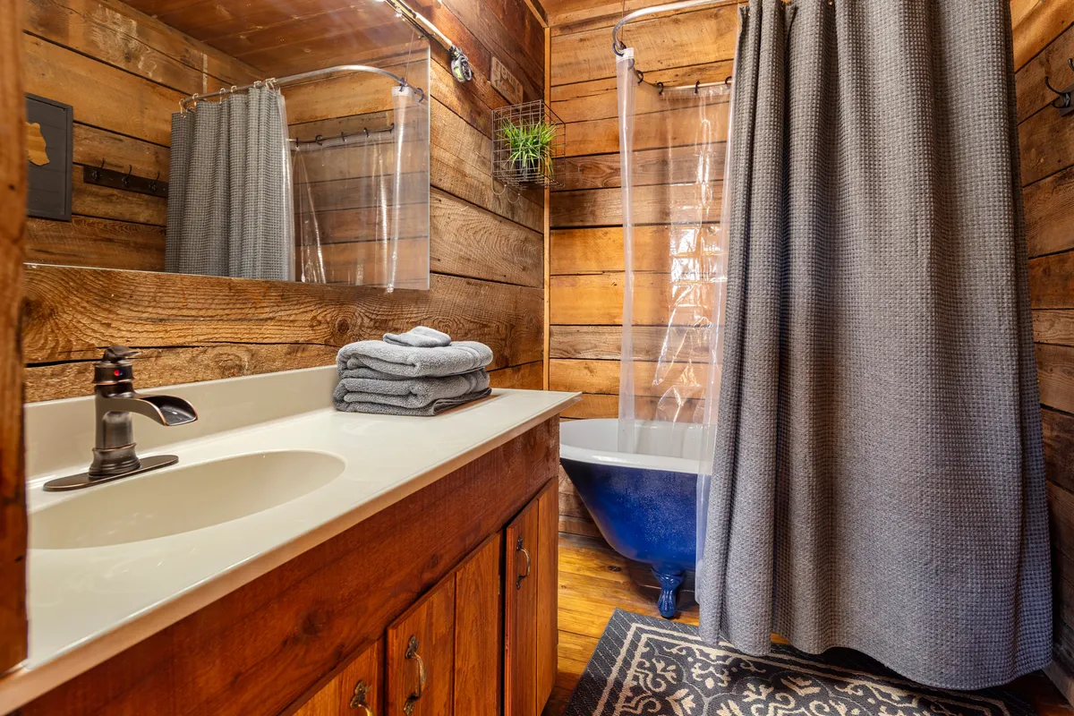 A stylish bathroom interior featuring rustic wooden walls, a freestanding vintage bathtub, a modern sink with a sleek faucet, and neatly folded towels. The space feels both tranquil and inviting, ideal for unwinding.